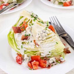 Savory wedge of iceberg lettuce topped with blue cheese dressing, crispy bacon, cherry tomatoes, and chives. Classic wedge salad for dinner or lunch.