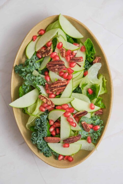 Fresh kale, pear, pomegranate, and pecan salad in a beige bowl.