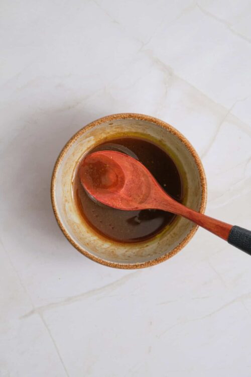 Soy sauce in a small bowl with a red spoon for cooking or dipping culinary sauces preparation.