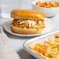 Soft, toasted sandwich bun filled with shredded chicken and creamy coleslaw on a white plate.