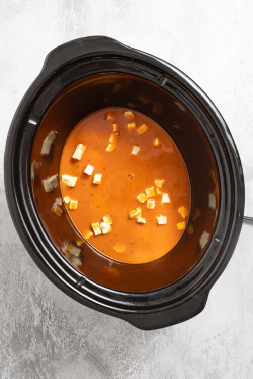 Creamy tomato soup in a slow cooker with cheese chunks, ready to serve.