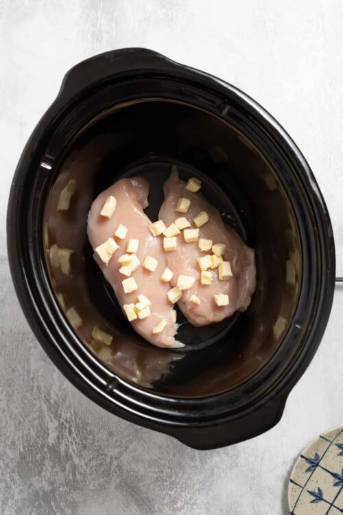 Boneless skinless chicken breasts with chopped garlic in a slow cooker.