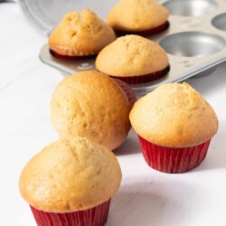 Freshly baked vanilla cupcakes in red paper liners on a white surface.