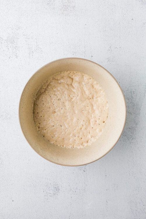 Creamy biscuit dough in a beige bowl on white textured surface.