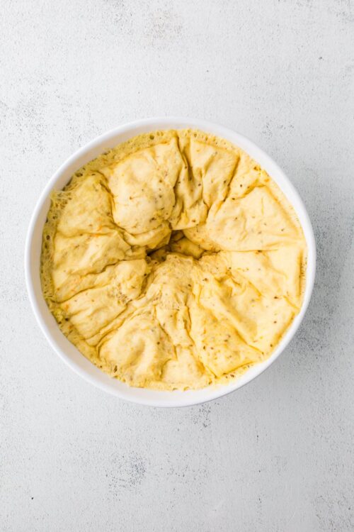Fluffy homemade baked cheese bread dough in a white bowl on a light textured background.