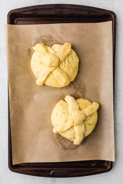 Soft pastry dough knot rolls on parchment paper baking sheet ready for oven baking.