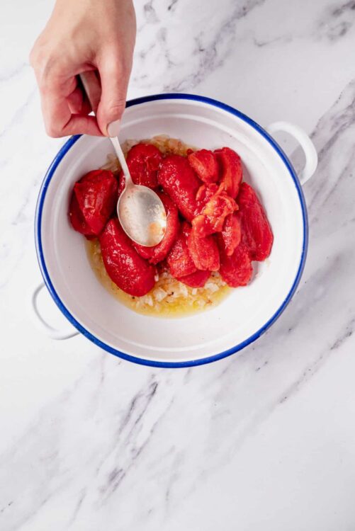 Sweet roasted tomatoes with garlic in a white bowl on marble surface.