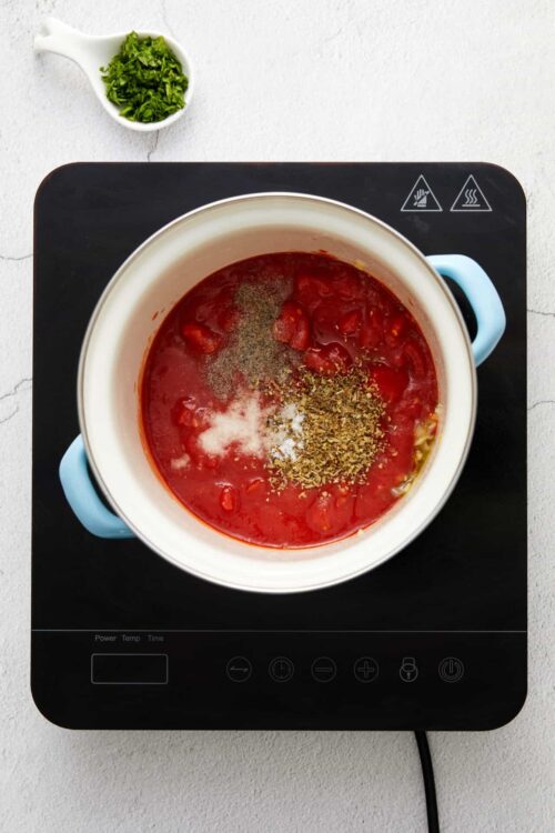 Chopped tomatoes with herbs and spices in a pot for homemade tomato sauce.