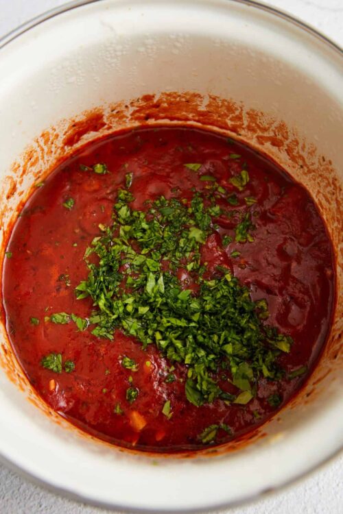 Rich homemade tomato soup garnished with fresh chopped herbs in a glass bowl.