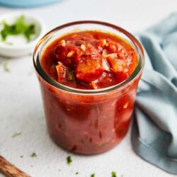 Savory homemade tomato sauce in a glass jar with chopped herbs and cooking spoon.