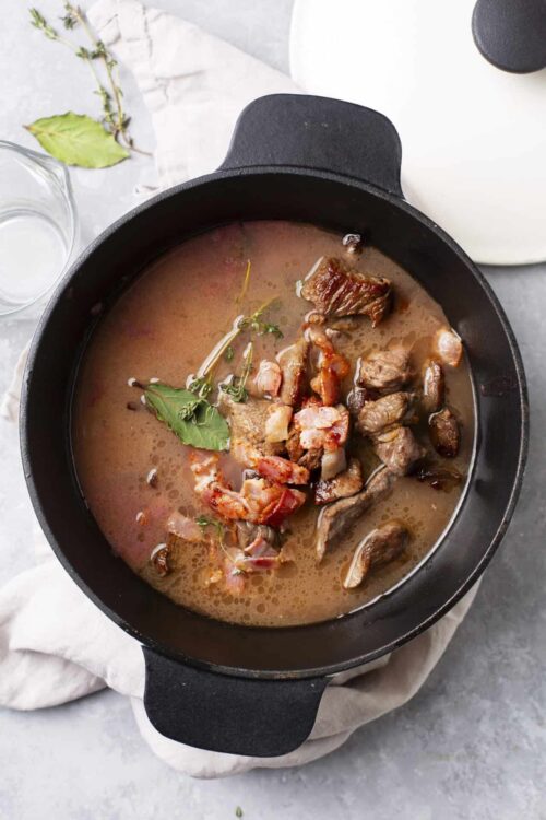 Beef stew in cast iron pot with vegetables and herbs.