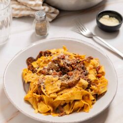 Comforting beef stew over homemade pasta on a white plate.