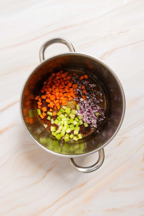Chopped carrots, celery, and onions sautéing in a stainless steel pot for soup.