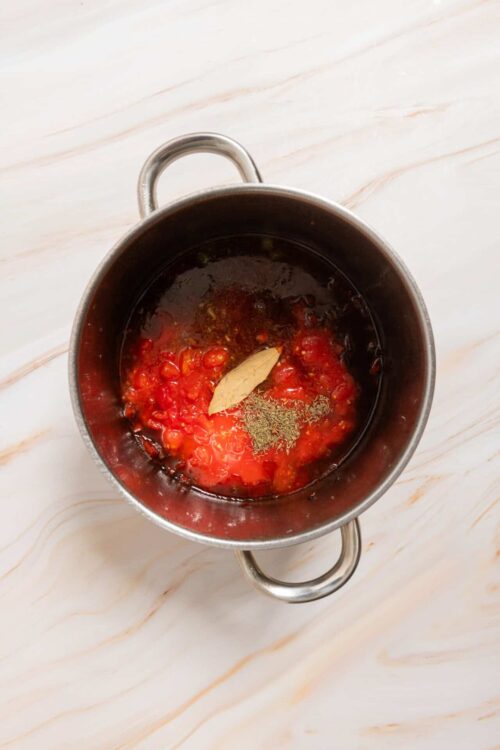 Cooked tomato sauce ingredients in a stainless steel pot with garlic and herbs.