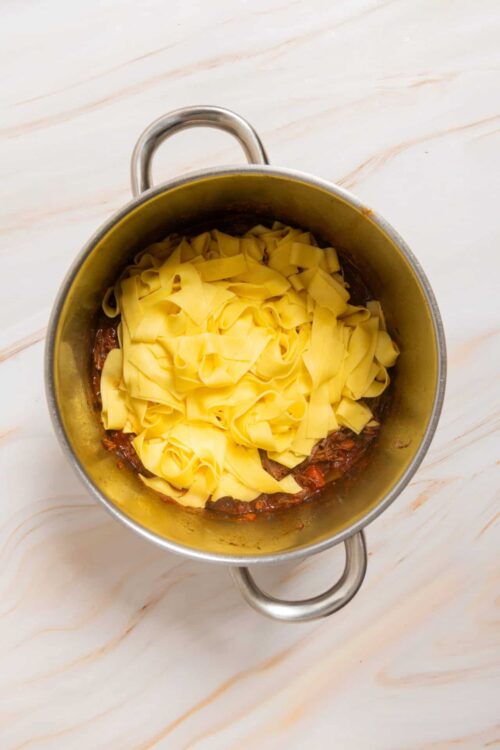 Rich beef stew with fresh pasta cooking in a stainless steel pot.