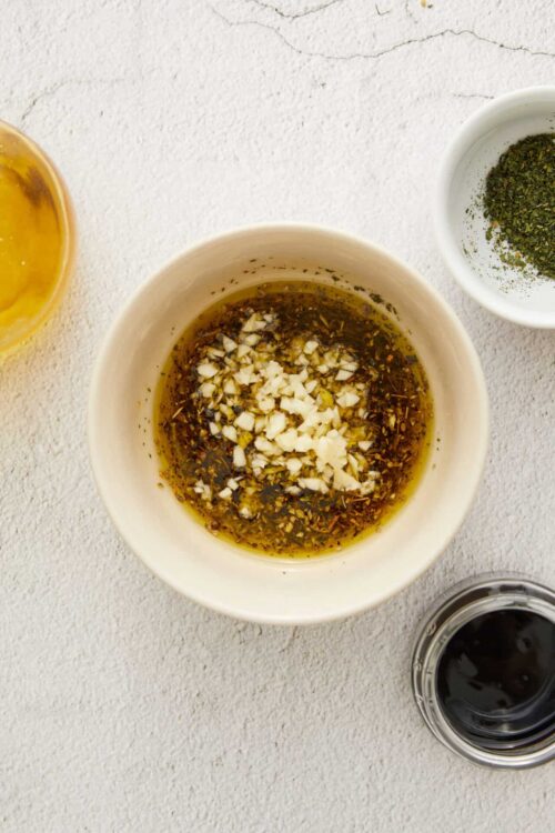 Vinaigrette ingredients including garlic, herbs, and oil in a white bowl.