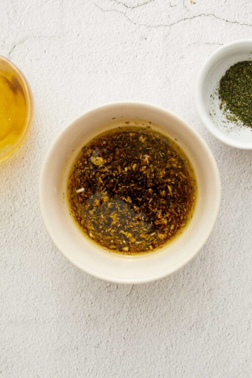 Seasoned herb and garlic oil mixture in a white bowl for baking or cooking.
