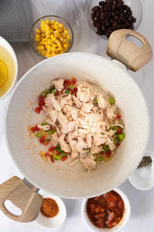 Cooked shredded chicken with diced red and green bell peppers in a white skillet, ready for a flavorful recipe.