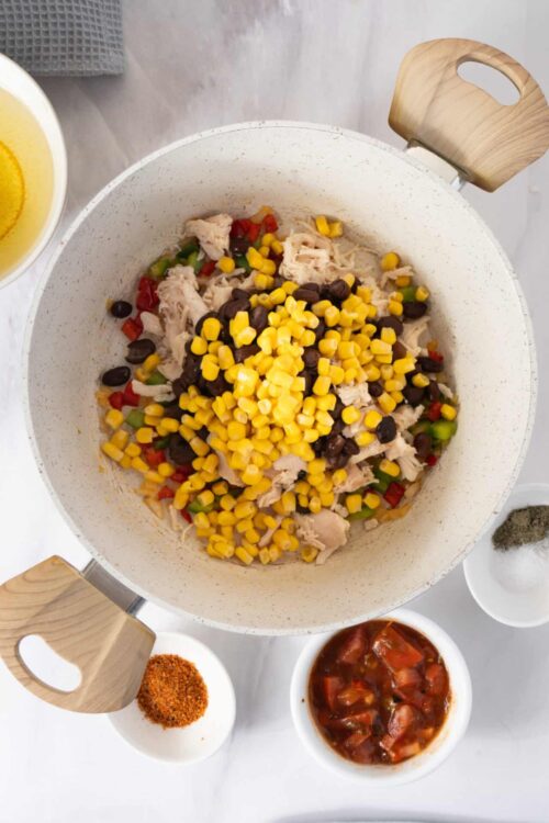 Cooked chicken corn and black bean mixture in a white pot with spices and vegetables ready for chili or casserole.