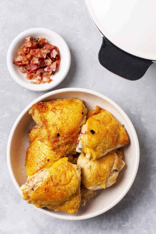 Golden roasted chicken thighs with crispy skin served with bacon bits and a side of creamy sauce. Perfect comfort food recipe from Baked Bree.