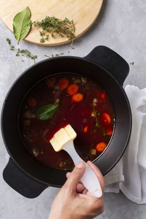 Broth with carrots and herbs in a pot ready for cooking.