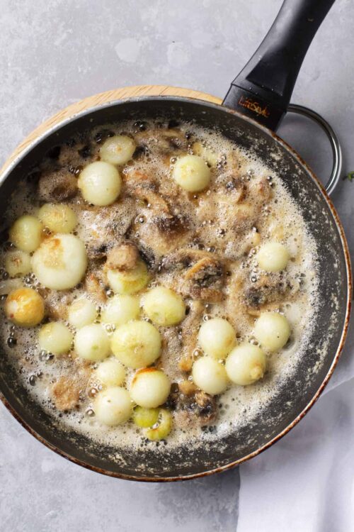 Creamy mushroom and pearl onion sauté in a skillet for flavorful comfort food.
