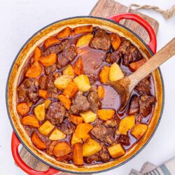 Hearty beef and vegetable stew in a cast iron Dutch oven with carrots, potatoes, and savory broth.