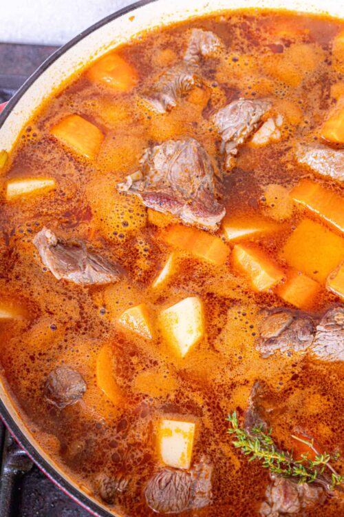 Savory beef stew with potatoes and herbs in a rich broth, close-up.