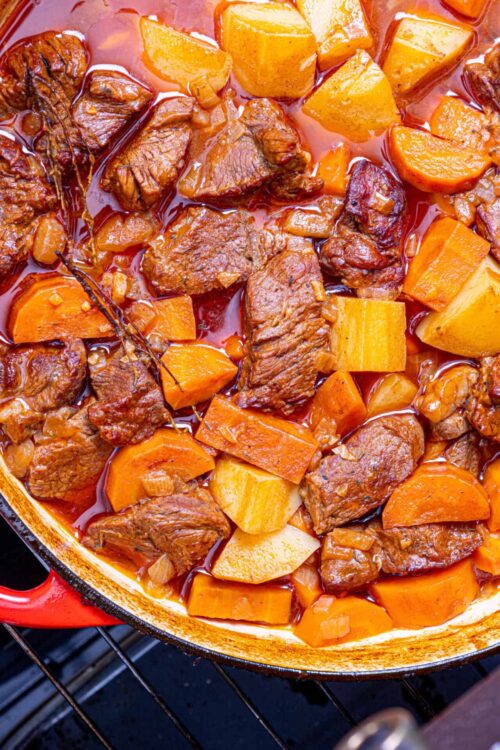 Beef stew with carrots and potatoes in a red Dutch oven pot.