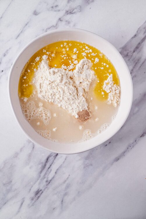 Flour, eggs, milk, and spices in a white bowl on marble surface for baking recipes.