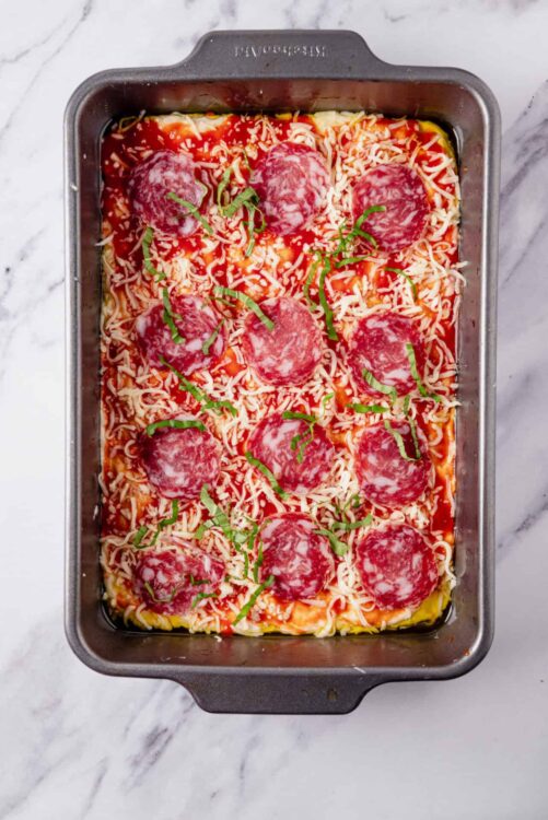 Baked pizza with pepperoni, cheese, and green herbs in a baking dish.