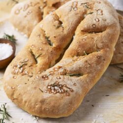 Flavored focaccia bread with rosemary and sea salt on baking paper.