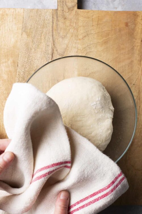 Soft pizza dough rising in a glass bowl with a towel, ready for baking.