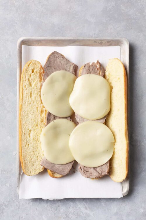 Thinly sliced roast beef sandwich with melted cheese on hoagie rolls, ready to assemble.