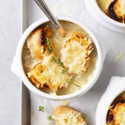 Creamy French onion soup with melted cheese and toasted croutons in white bowls.