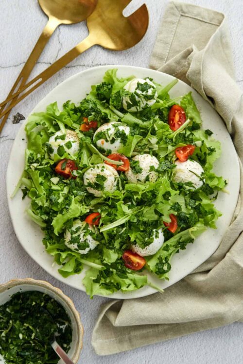 Fresh mozzarella caprese salad with cherry tomatoes, basil, and mixed greens on a white plate for a healthy recipe.