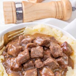 Savory beef stew over mashed potatoes in white bowl.