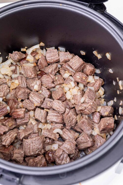 Cube-cut beef in an instant pot with sautéed onions.