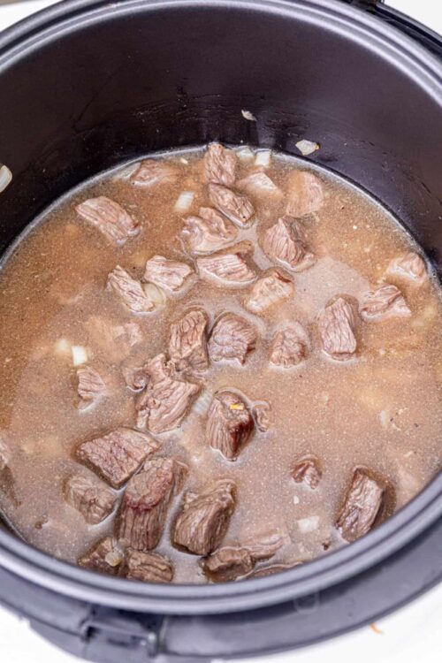 Slow cooker beef stew cooking in a black slow cooker.