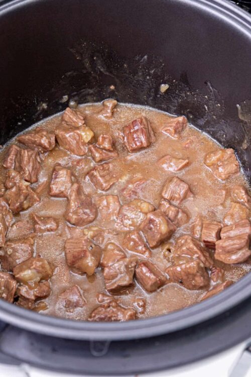 Tender beef cooking in a slow cooker with savory gravy for delicious beef stew.