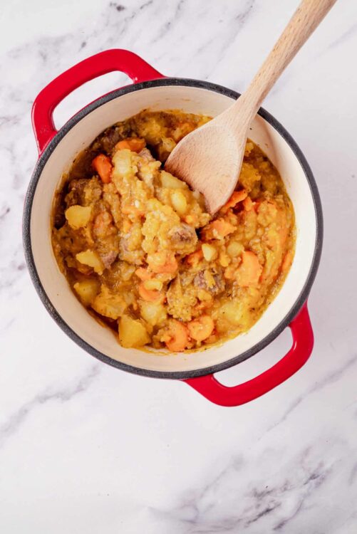 Creamy beef and vegetable stew in a red cast iron pot with a wooden spoon, comforting homemade dinner.