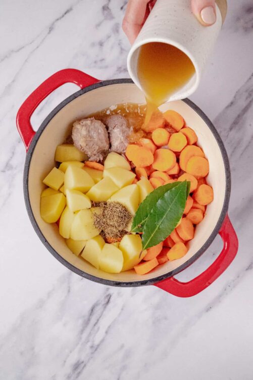 Butternut squash, carrots, potatoes, and herbs in a Dutch oven for soup.