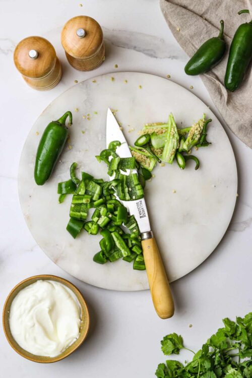 Chopped jalapeños and fresh peppers on a marble cutting board with a chef’s knife.