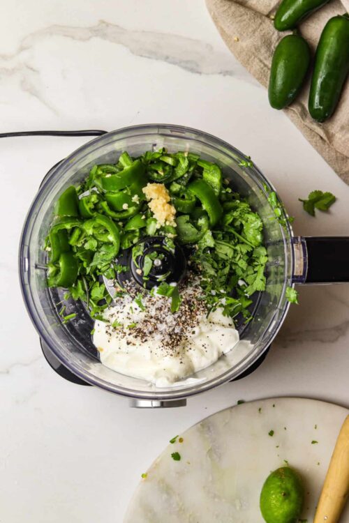 Fresh green jalapeño peppers, garlic, cilantro, and spices in a food processor for spicy jalapeño sauce.