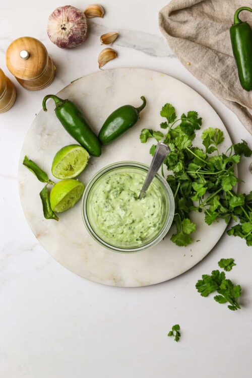 Creamy cilantro lime dressing with fresh jalapeños and lime on a marble cutting board.