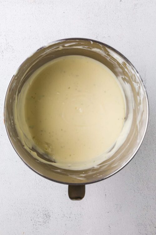Creamy white sauce in a stainless steel mixing bowl with a slightly textured white background.