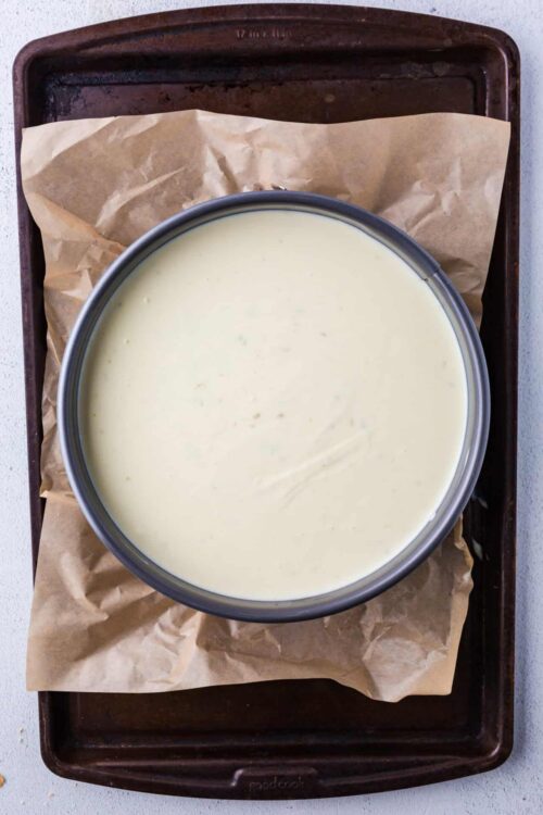 Creamy cheesecake batter in a metal bowl on parchment-lined baking sheet.