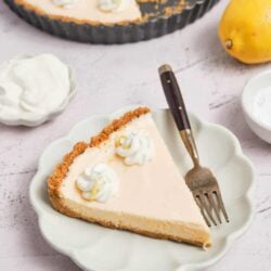 Creamy lemon cheesecake with graham cracker crust on a white plate.