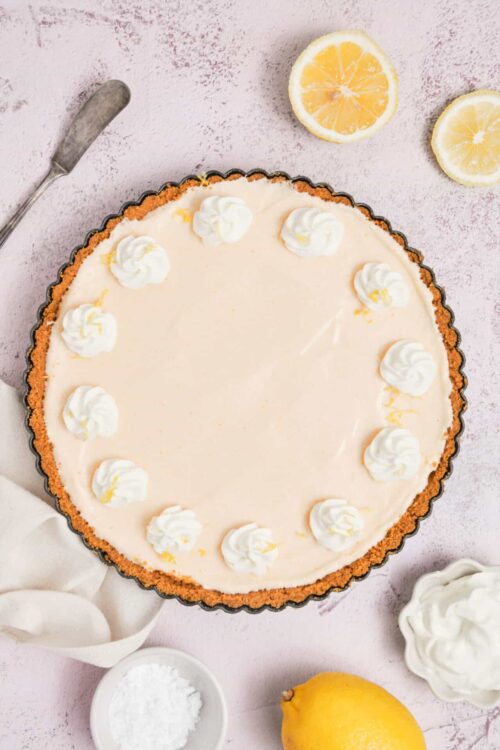 Lemon cheesecake with whipped cream toppings on a pink textured background.
