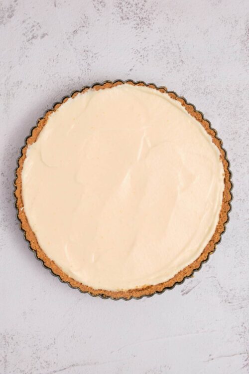 Cream cheese tart with a graham cracker crust on white background.